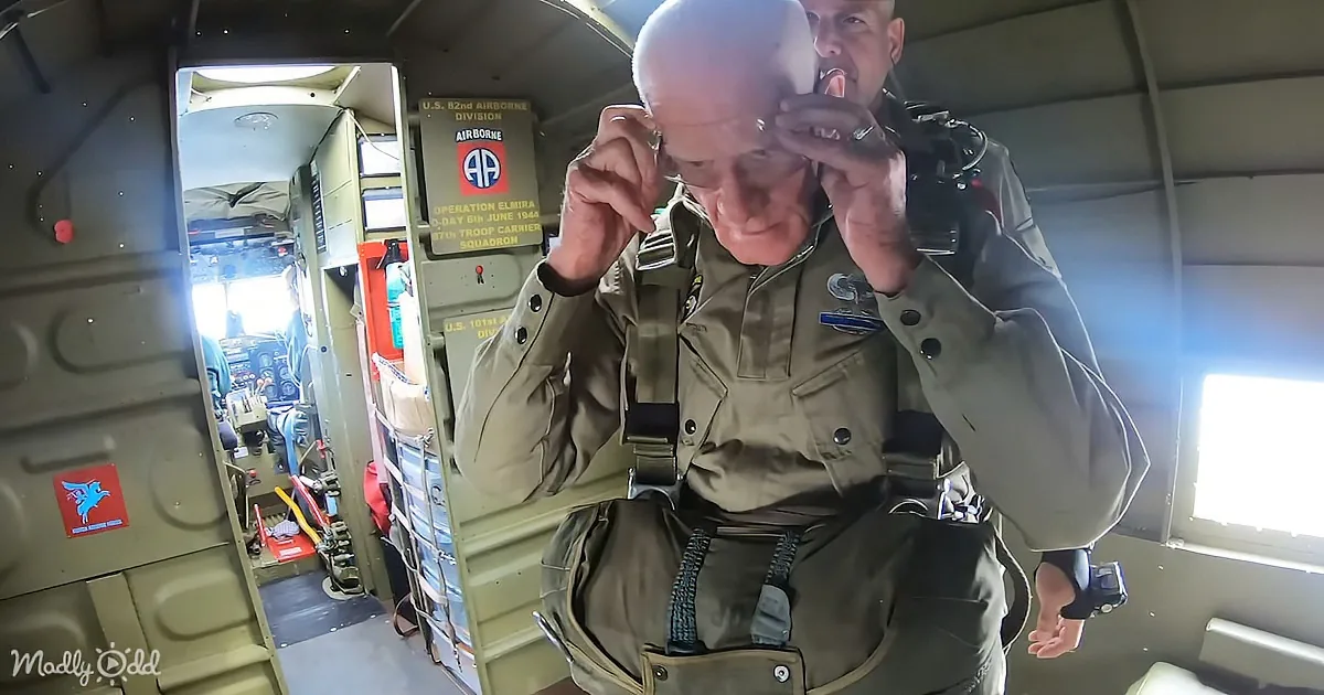 An older man in military attire adjusts his goggles inside a military aircraft.