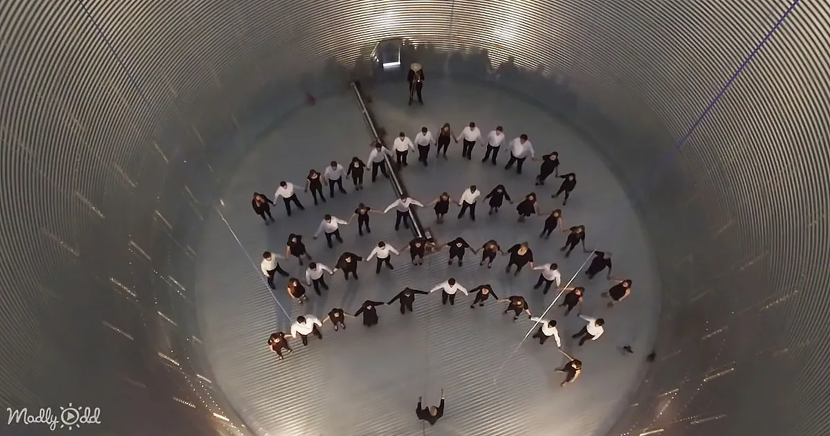 A group of people in a circle holding hands inside a large, metallic, cylindrical structure.
