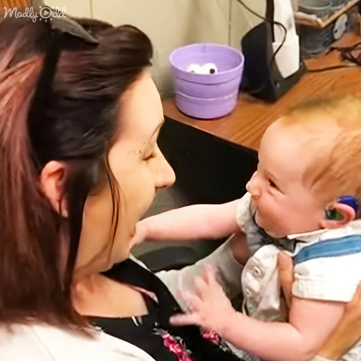 A woman holds a baby with a hearing aid, both smiling and interacting closely.