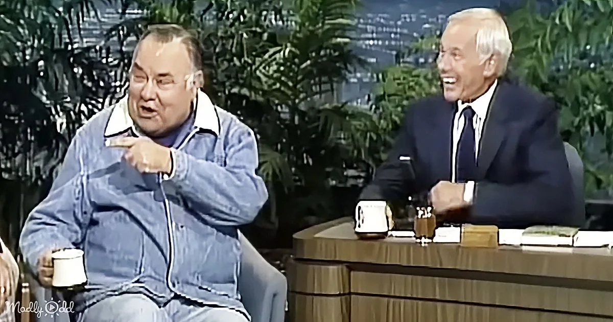 A man in a denim jacket points emphatically while another man in a suit laughs, both seated on a talk show set.