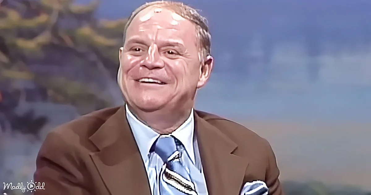 A man in a brown suit and blue striped tie smiles against a scenic background.