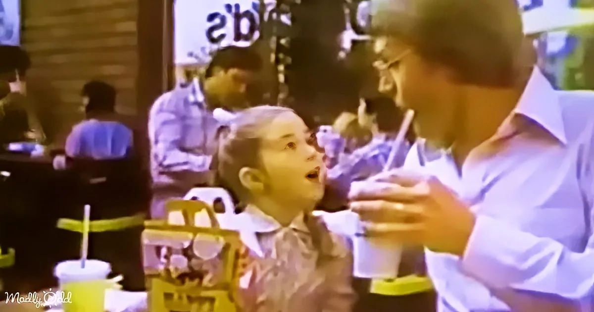 A man in a white shirt holds a drink, while a child in a pink shirt looks up, both in a restaurant setting.
