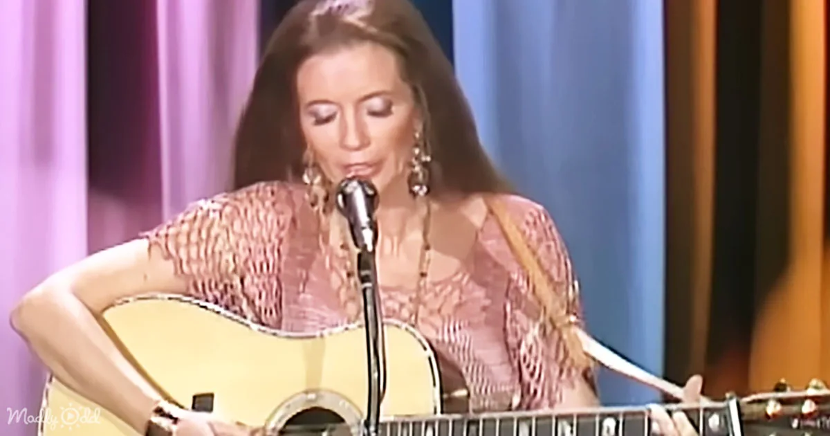 A woman in a pink dress plays an acoustic guitar on stage with a microphone.
