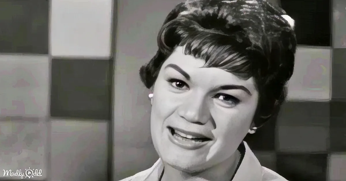 A woman with short, styled hair smiles, wearing earrings, in a black-and-white setting.