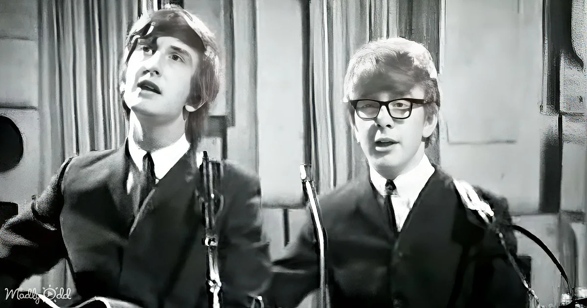Two men in suits, one with glasses, singing into microphones in a vintage setting.