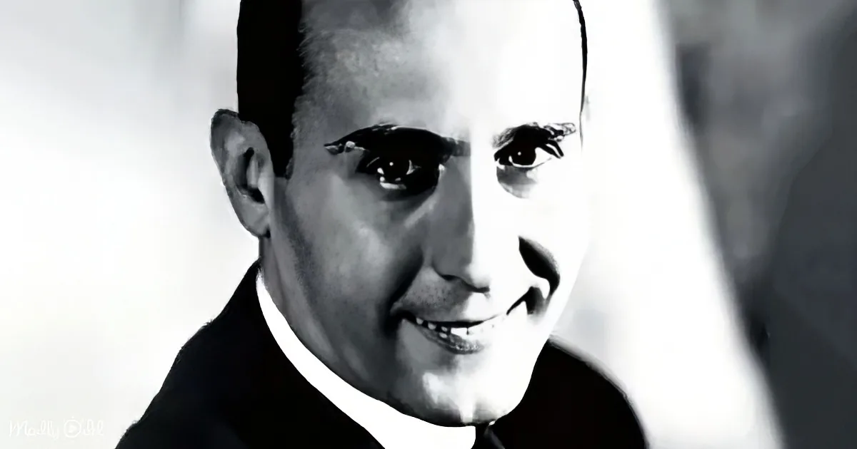 A man in a suit and tie smiles, looking to the side, in a black-and-white portrait.