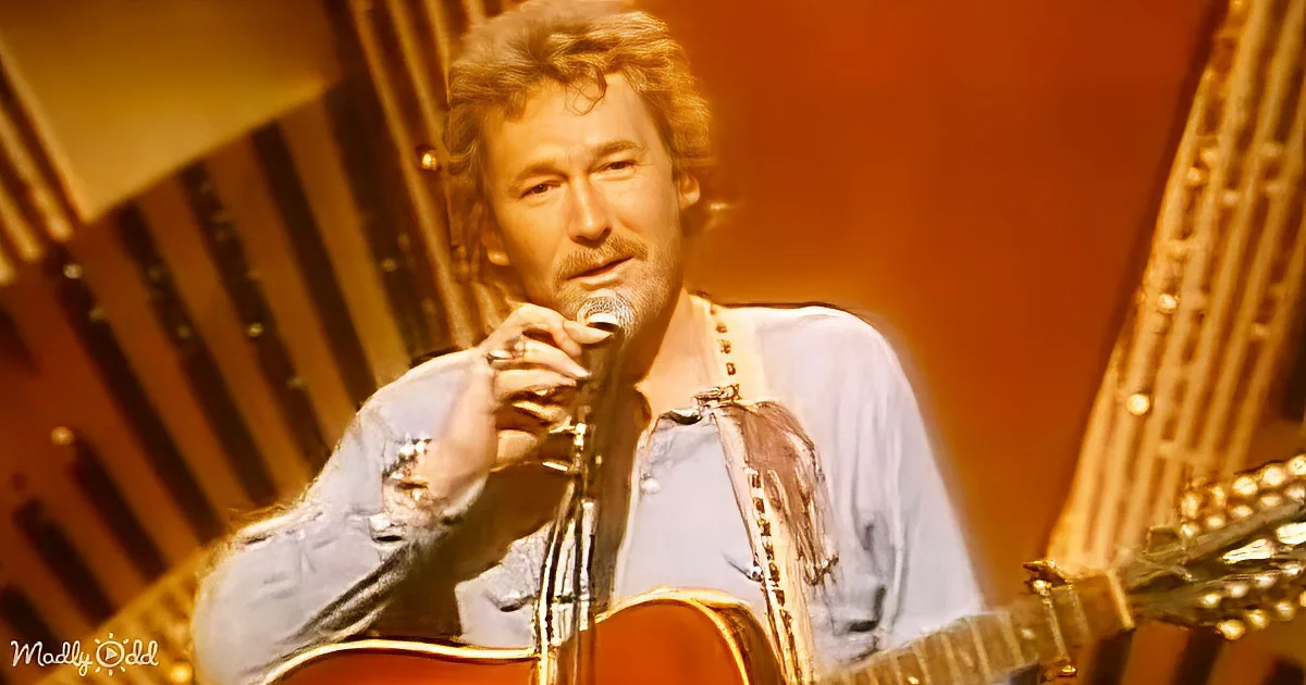 A man with curly hair and a beard holds a microphone and guitar, wearing a light blue shirt with suspenders.