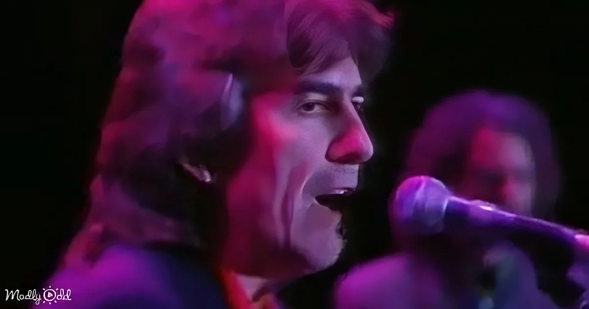 A person with long hair and a microphone, illuminated by purple and pink stage lights.