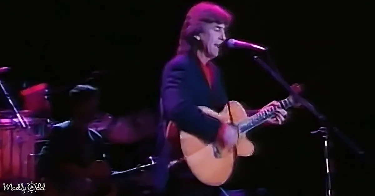 A person plays guitar and sings into a microphone on stage, illuminated by purple light.