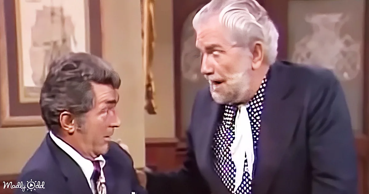 An older man in a suit and tie is speaking to another man in a suit, both in a formal setting.
