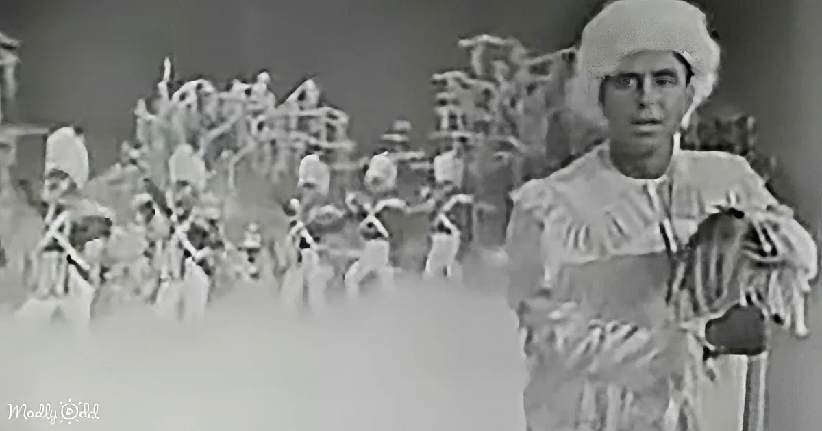A man in traditional attire stands in front of a crowd, possibly in a historical or theatrical setting.