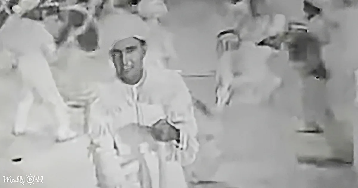 A man in a white robe sits surrounded by people in white, possibly in a religious or ceremonial setting.