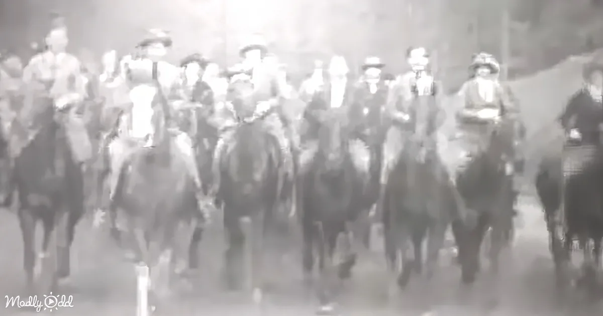 A group of people on horseback, dressed in old-fashioned attire, are riding through a dusty environment.