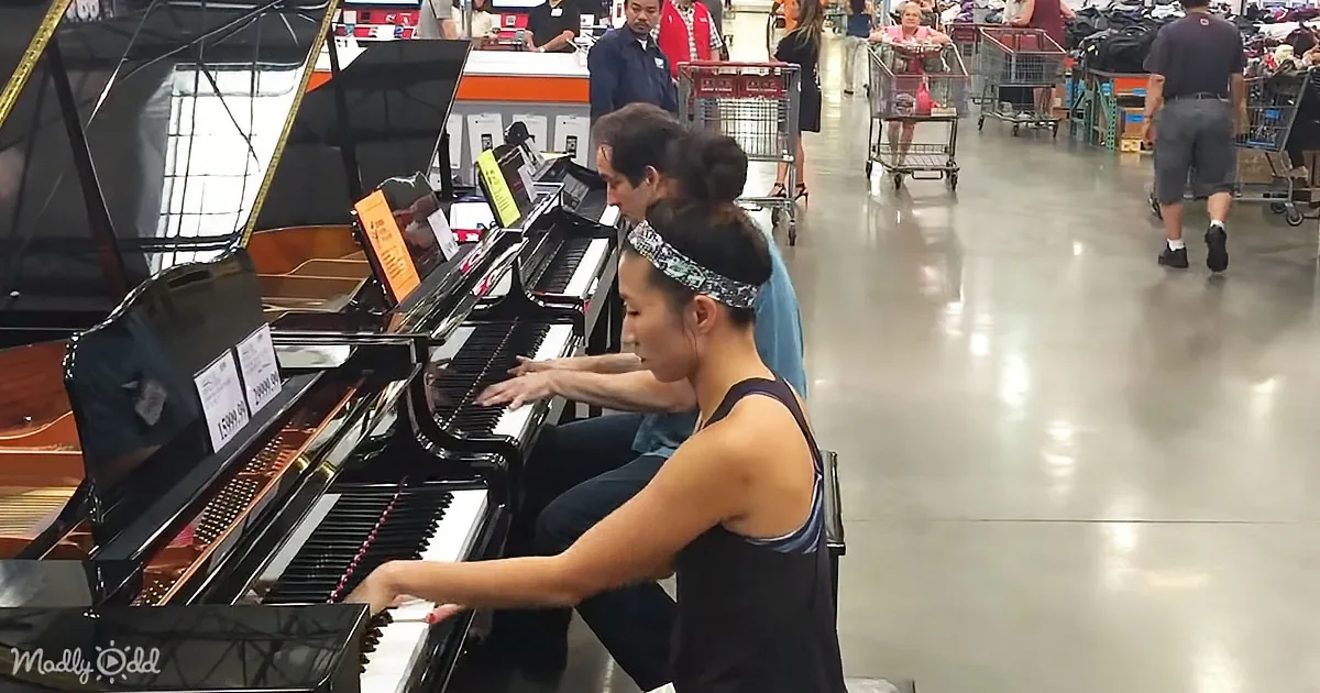 A woman plays a grand piano in a store aisle, surrounded by shoppers and shopping carts.