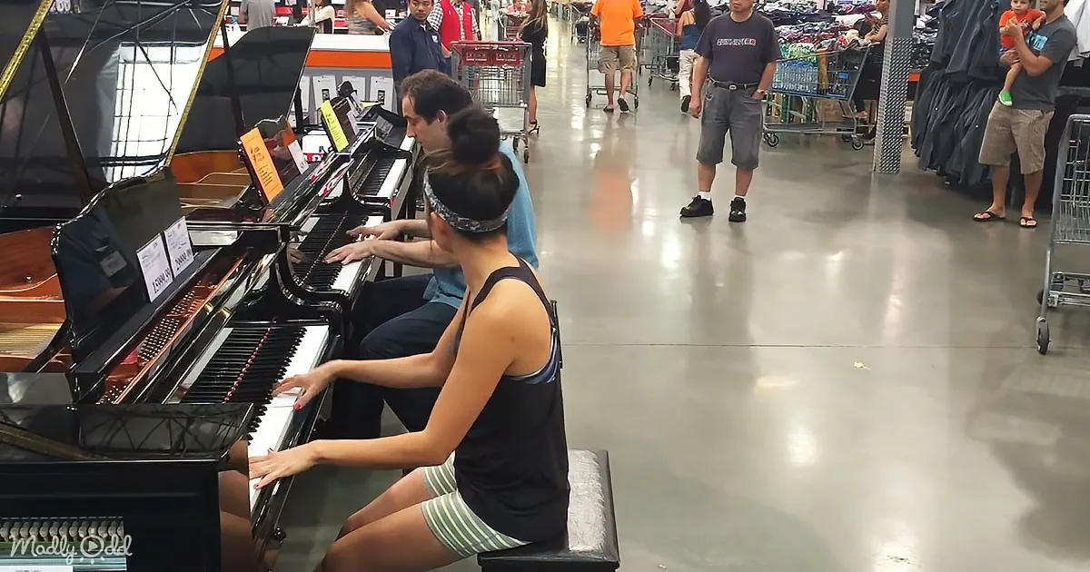 A woman plays a piano in a store aisle, surrounded by shoppers and shopping carts.
