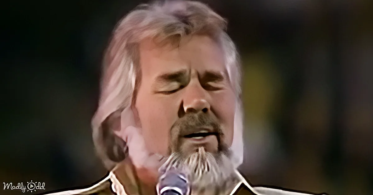 A man with long white hair and beard sings into a microphone, eyes closed, in a close-up shot.