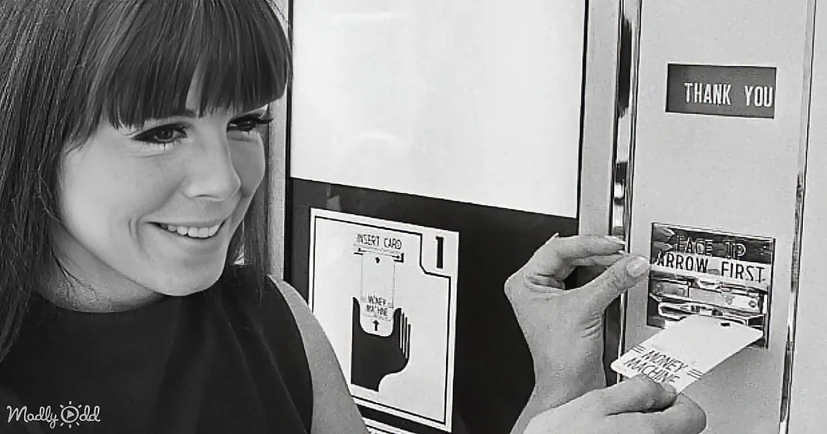 A smiling woman inserts a card into a vintage ATM machine.