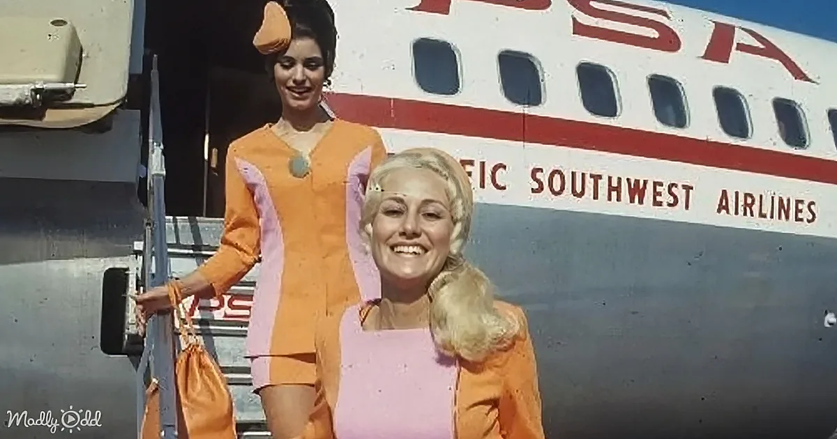 Two women in orange and pink uniforms stand in front of a Southwest Airlines plane.