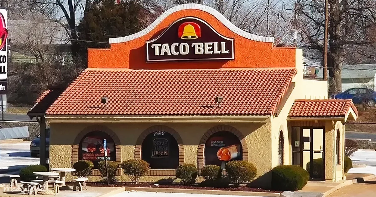A Taco Bell restaurant with a red-tiled roof and arched windows, surrounded by bare trees and a clear sky.