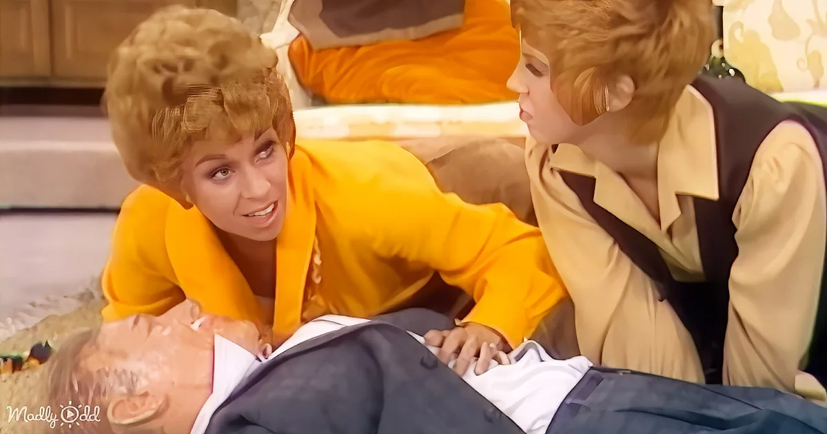 A woman in a yellow outfit leans over a man in a suit, appearing concerned or curious.