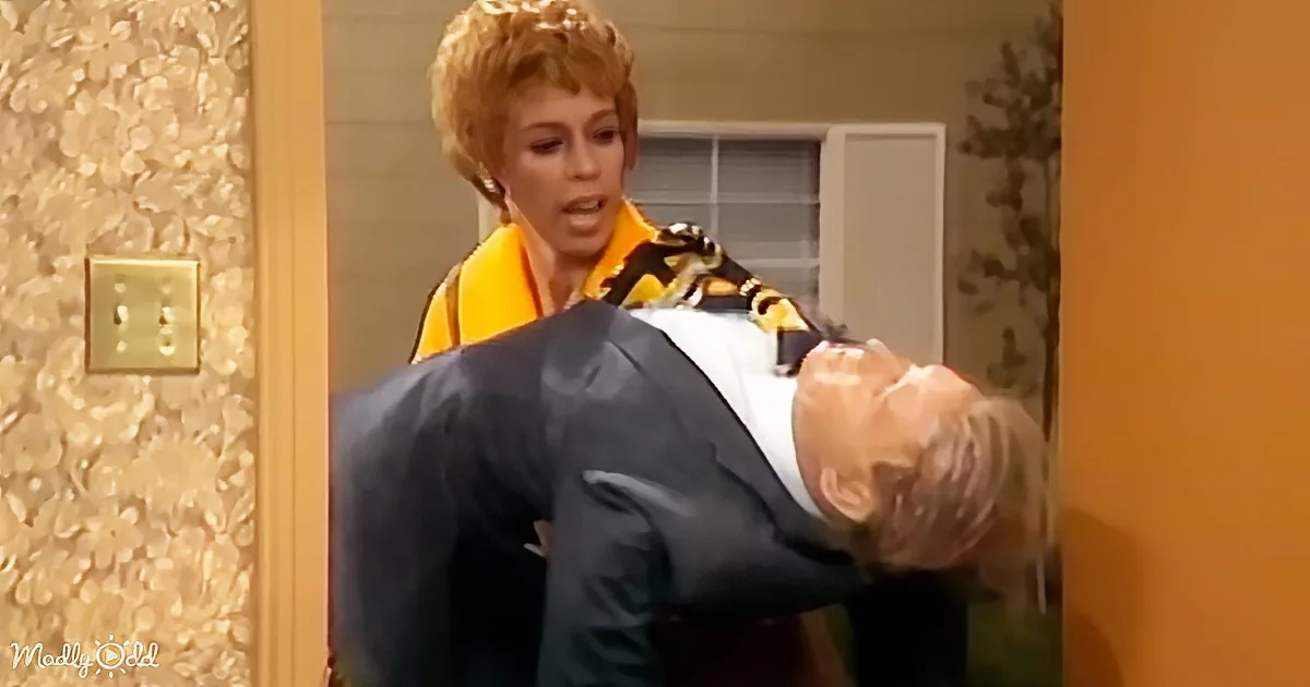 A woman in a yellow top holds a man in a suit by his neck, appearing to struggle.