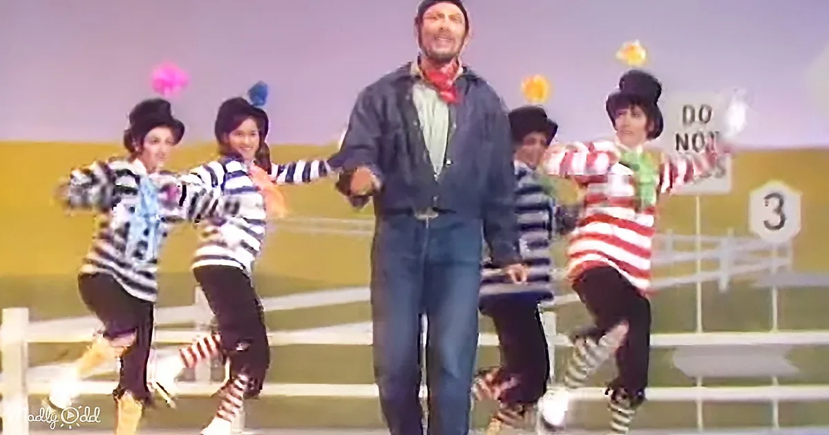 A man in a denim outfit leads a group of dancers in a lively performance.