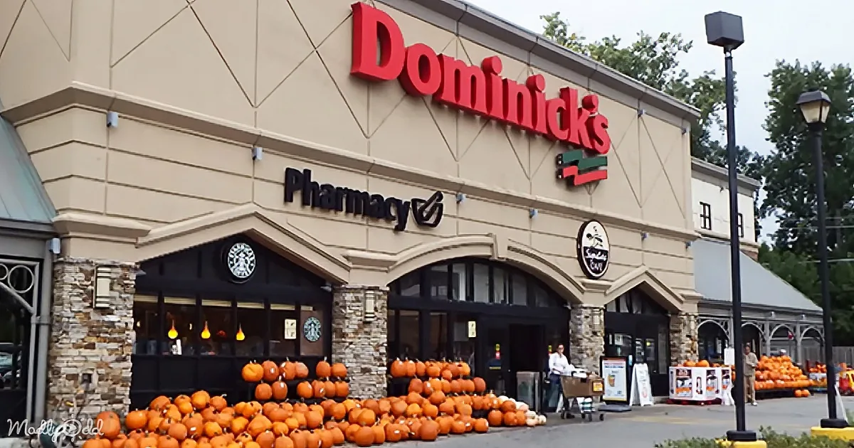 Dominick's Pharmacy storefront with pumpkins displayed outside, a Starbucks sign above, and a person pushing a cart.