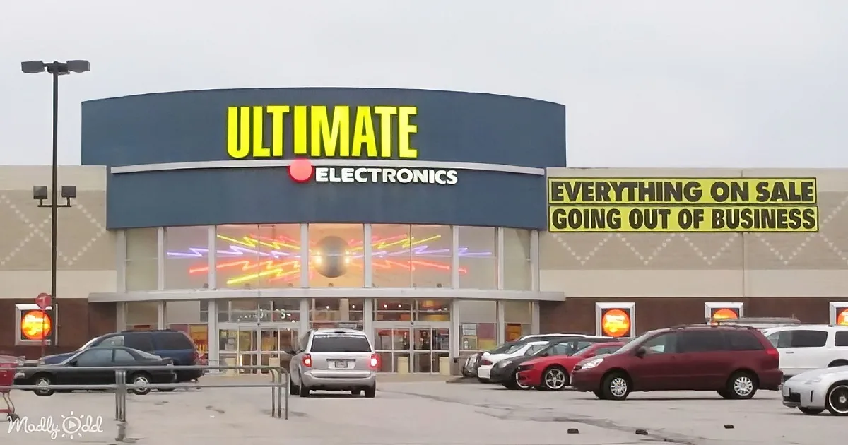 Ultimate Electronics store with "Everything on Sale Going Out of Business" sign, cars in parking lot, overcast sky.