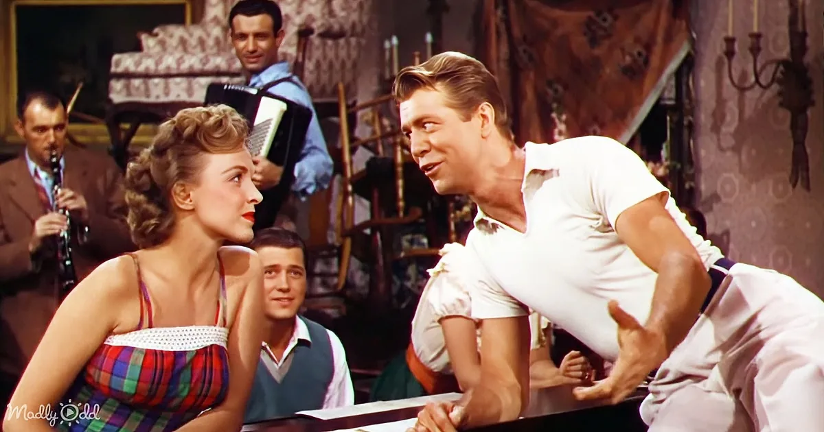 A man in a white shirt leans forward, engaging with a woman in a plaid dress at a table, surrounded by musicians.