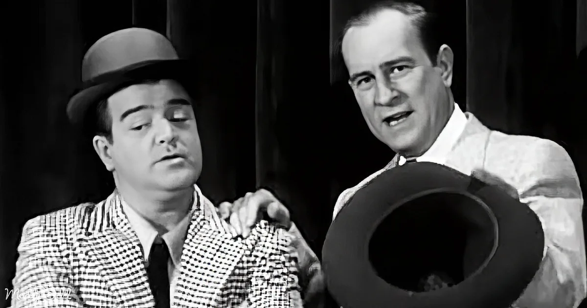 A man in a checkered suit and hat is being patted on the shoulder by another man holding a hat.