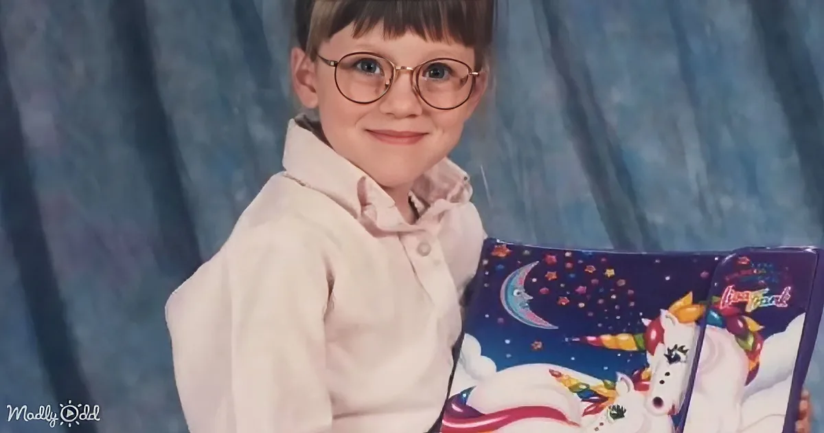 A young child wearing glasses holds a colorful unicorn-themed book against a blue backdrop.