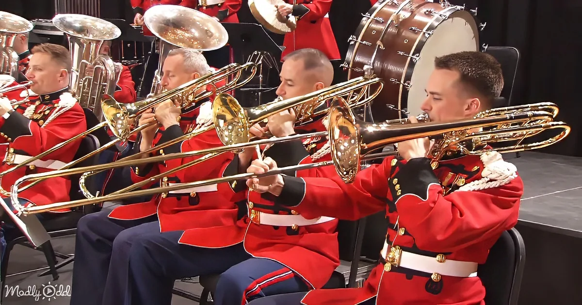 Four men in red uniforms play trombones in a military band ensemble.
