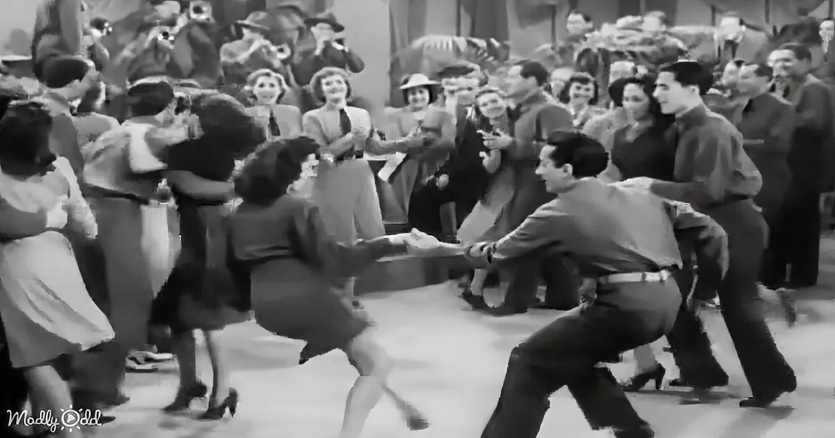 A man and woman dance in a lively scene, surrounded by a crowd watching and clapping.