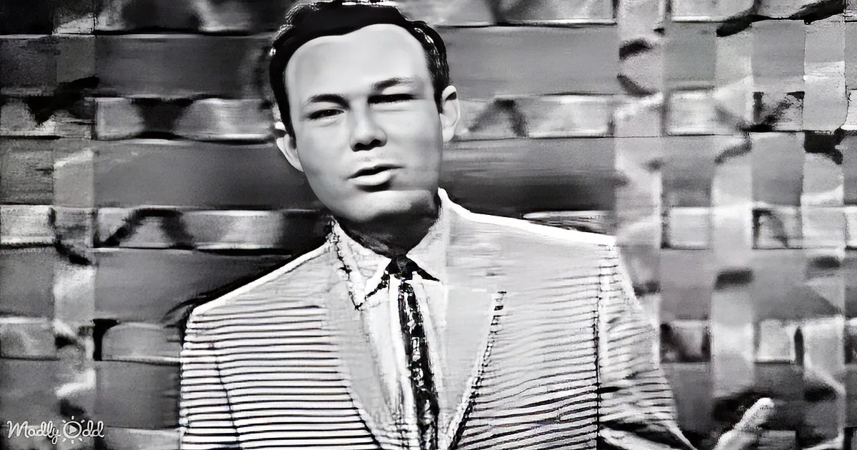 A man in a striped suit and tie stands against a brick wall backdrop.