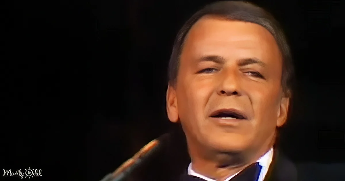 A man in a suit sings into a microphone against a dark background.