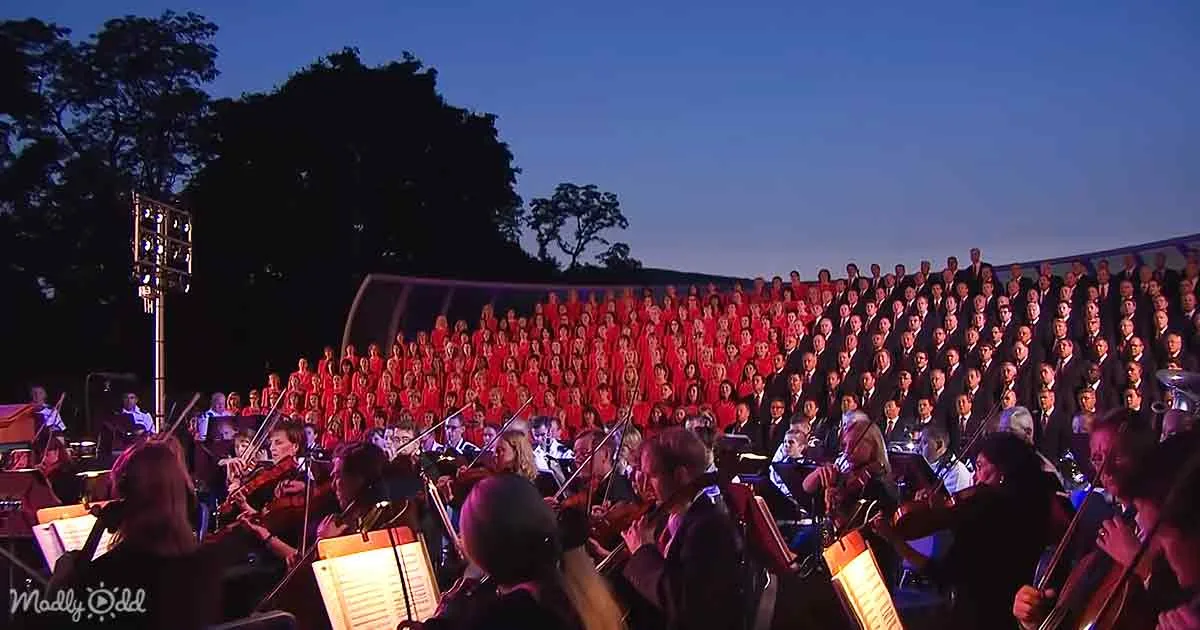 A large choir in red and an orchestra in black performing under a night sky.