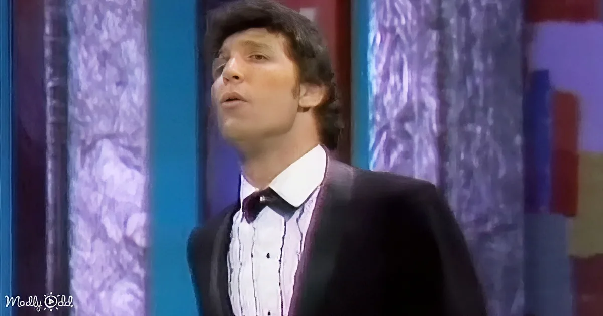 A man in a suit and bow tie looks upwards, with a colorful, patterned background.