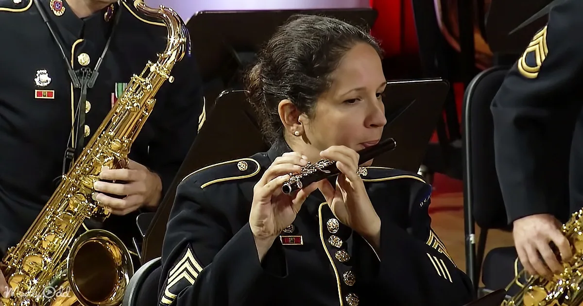 A woman in a military uniform plays a flute in a band setting.