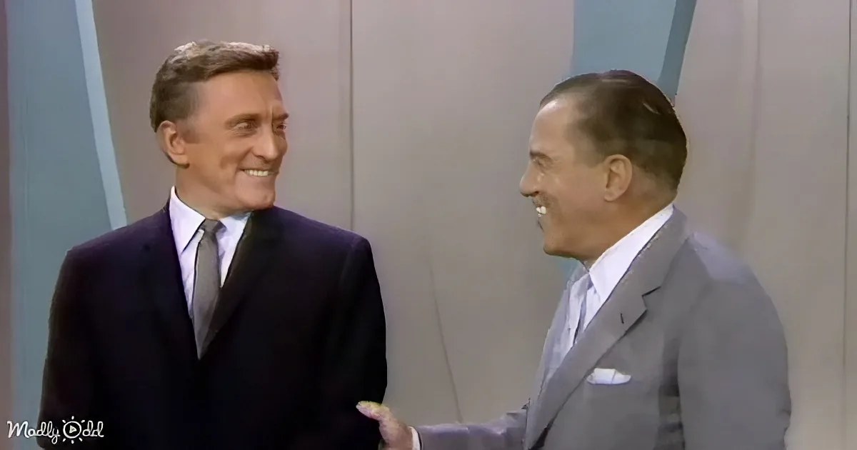 Two men in suits are smiling and talking, one gesturing with his hand.