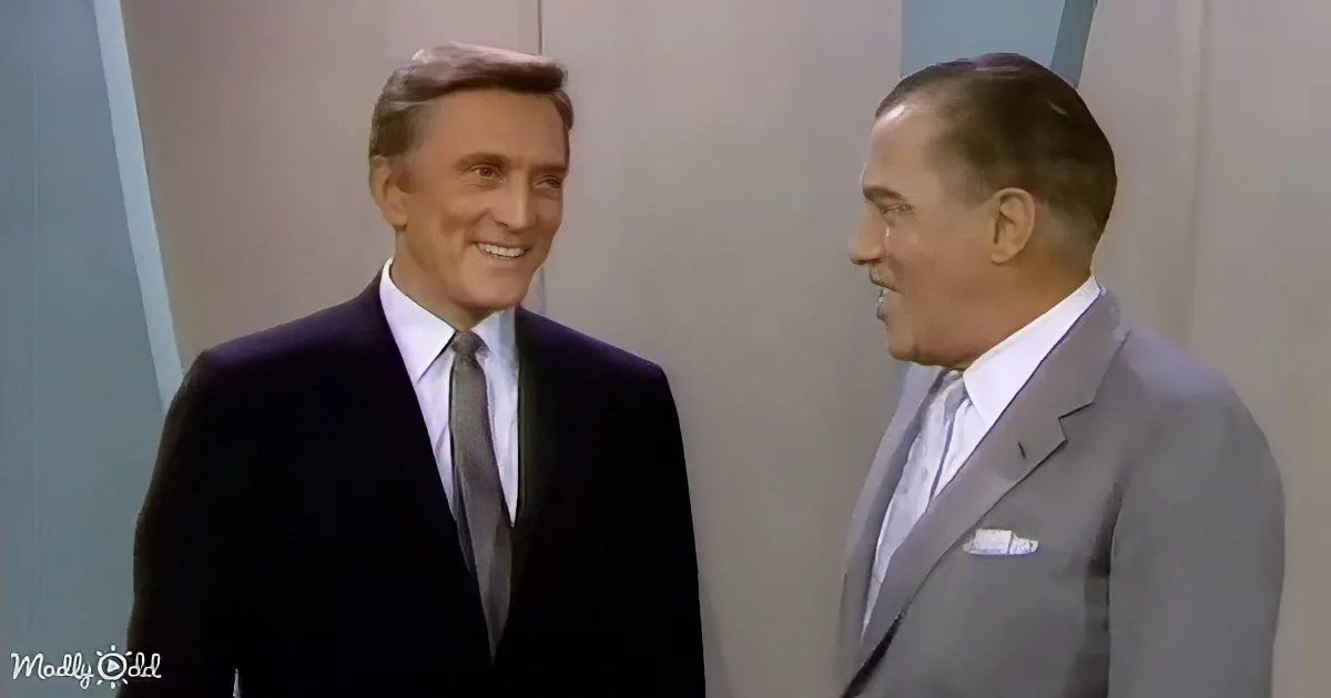 Two men in suits are smiling and talking, one in a dark suit and the other in a light gray suit.