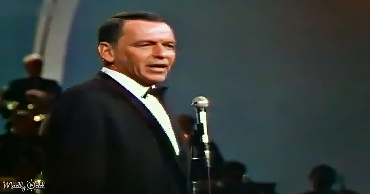 Frank Sinatra in a suit singing into a microphone on stage.