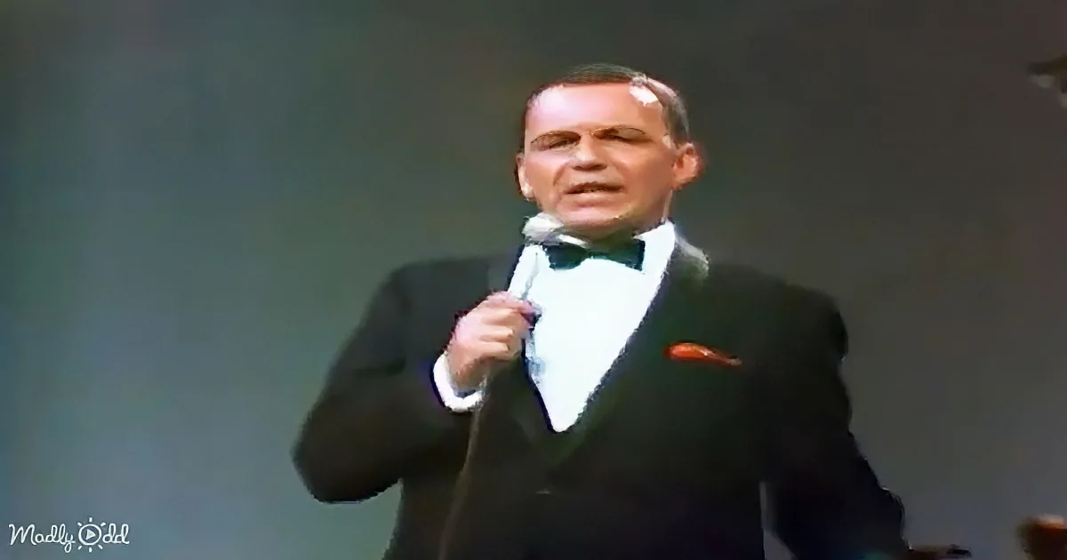 A man in a tuxedo holding a microphone, possibly singing or speaking on stage.