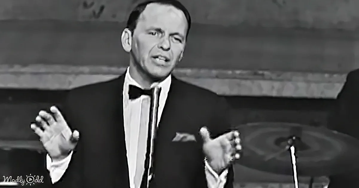 Frank Sinatra in a tuxedo, gesturing with his hands, appears to be singing or speaking on stage.