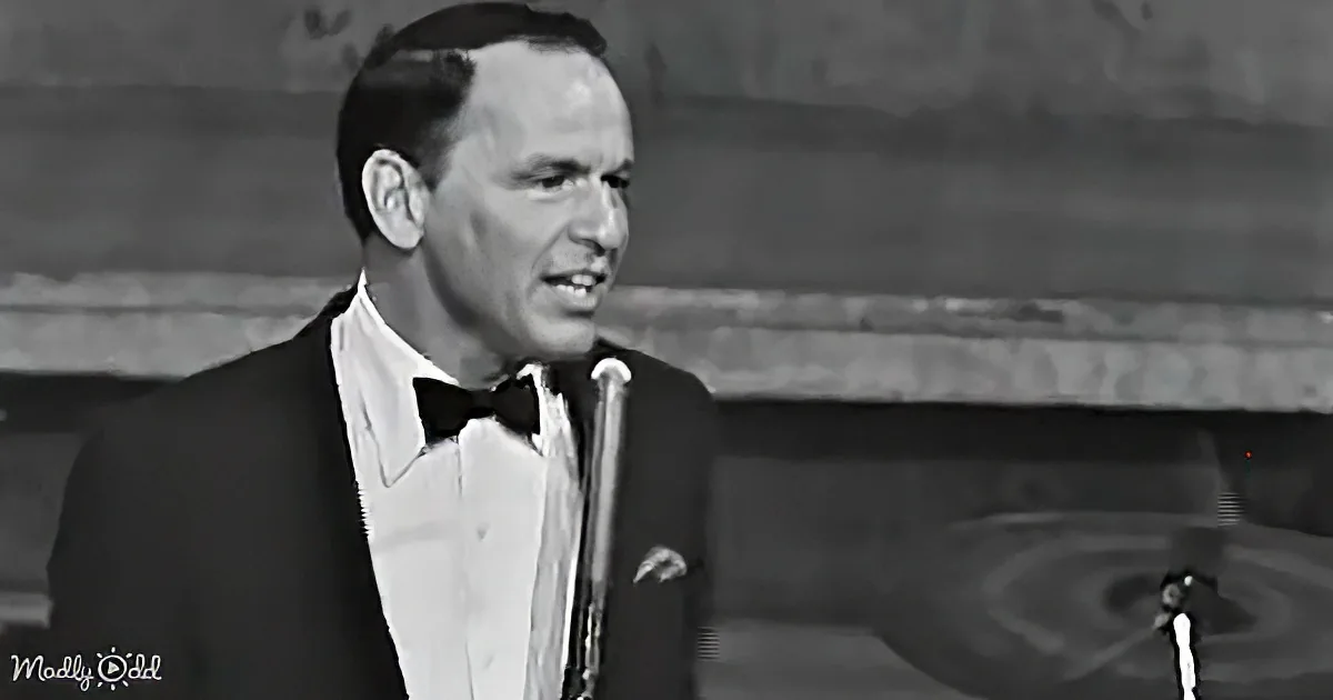 A man in a tuxedo sings into a microphone, with a blurred background and a watermark.