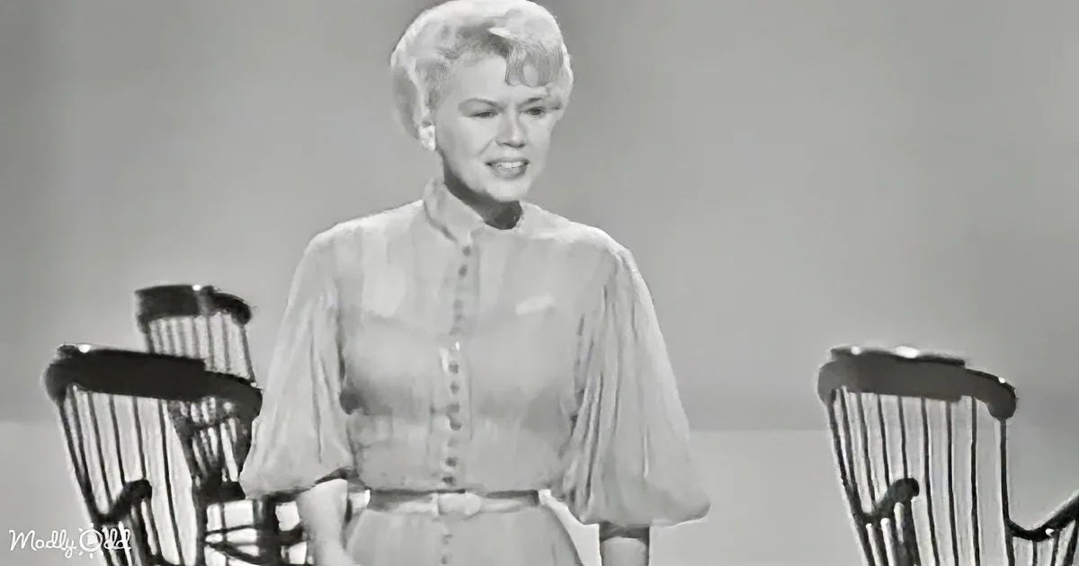 A woman in a vintage dress stands between two chairs, smiling.