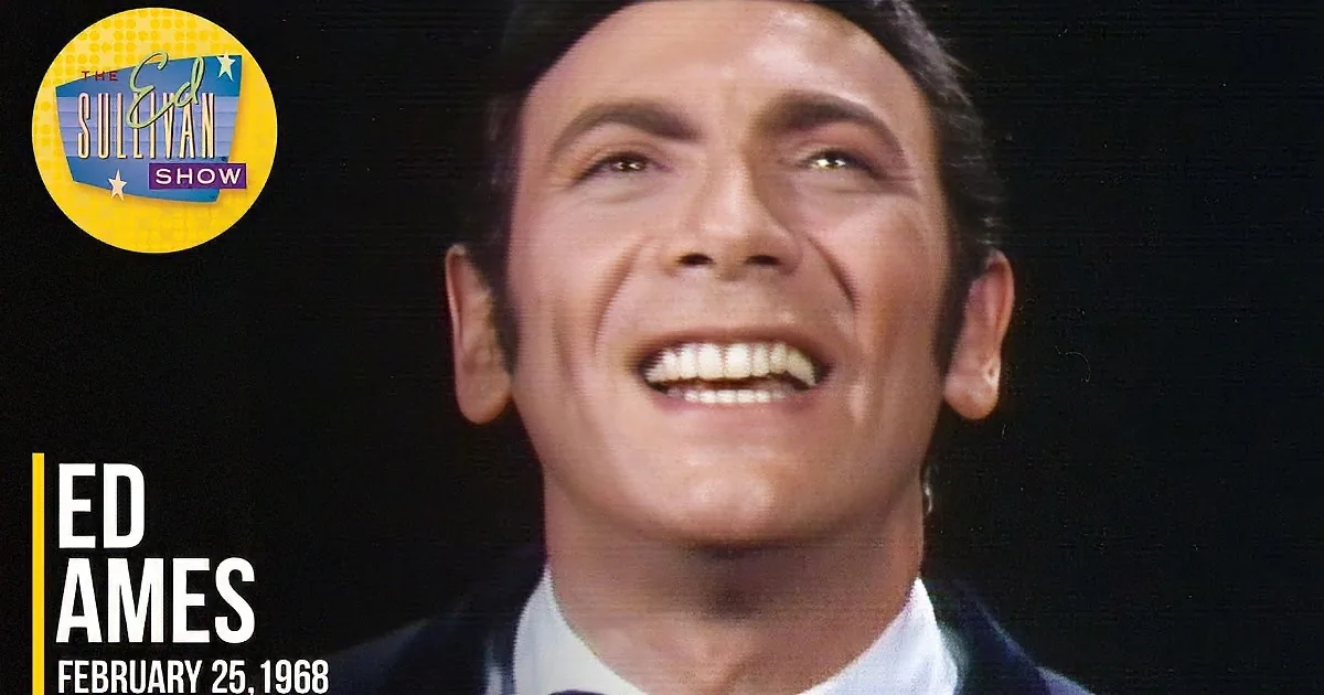 A man in a suit smiles warmly, his eyes crinkled in a genuine expression.