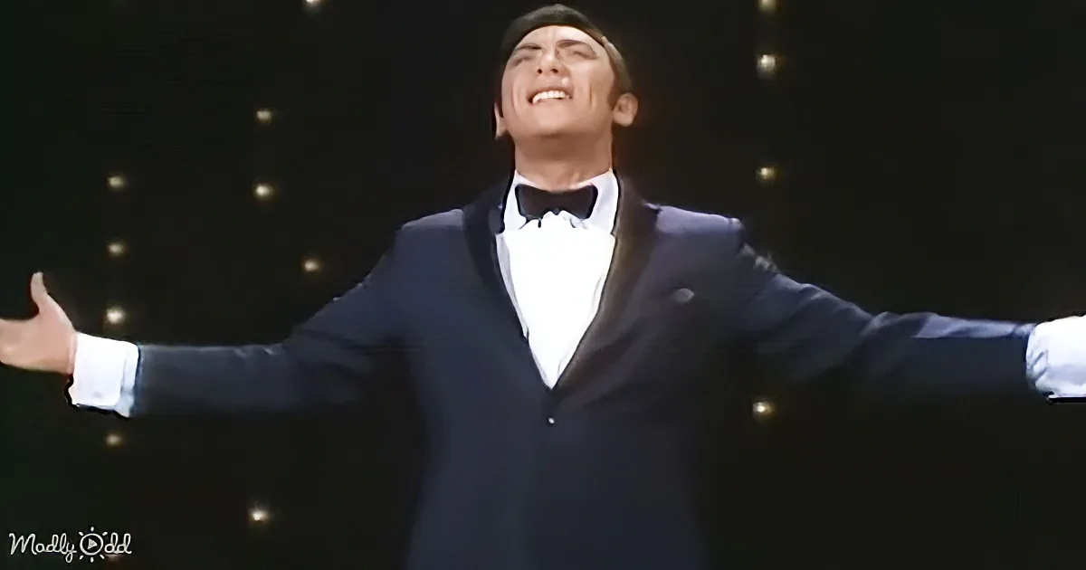 A man in a tuxedo with arms outstretched, smiling, and wearing a bow tie.