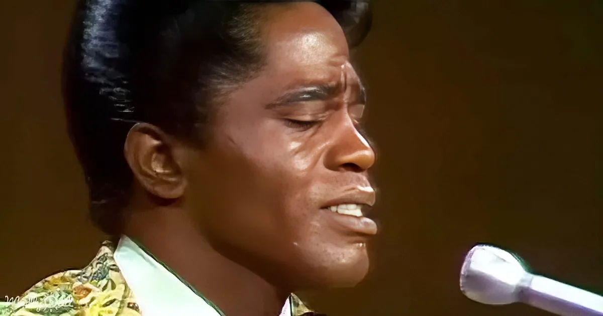 A man with slicked-back hair and a colorful patterned suit sings into a microphone.