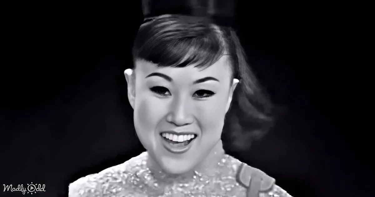A smiling woman with short hair and a patterned top, set against a dark background.