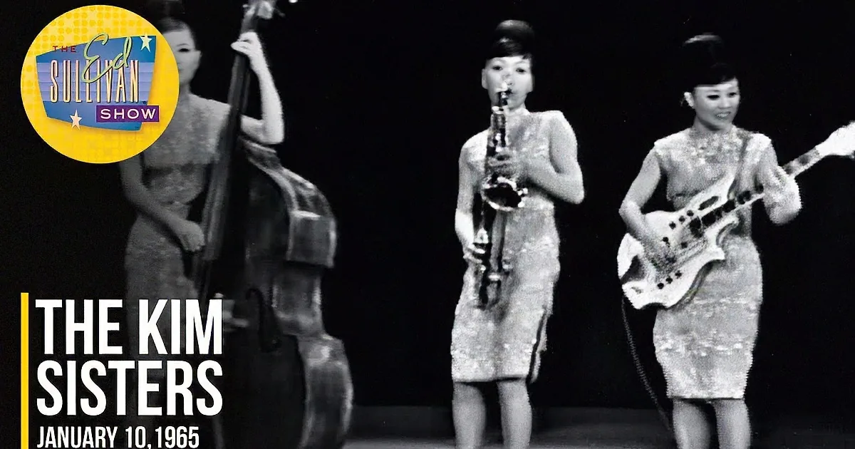 Three musicians in traditional attire perform on stage, one playing a string instrument, another a saxophone, and the...